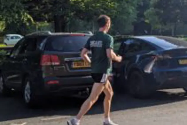 A man in a green tshirt runs to the right in front of two cars
