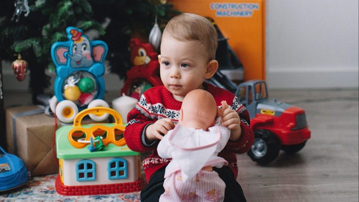 Young child playing with a doll by a Christmas tree