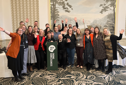 A group of people with arms raised celebrate in a room with a fancy carpet