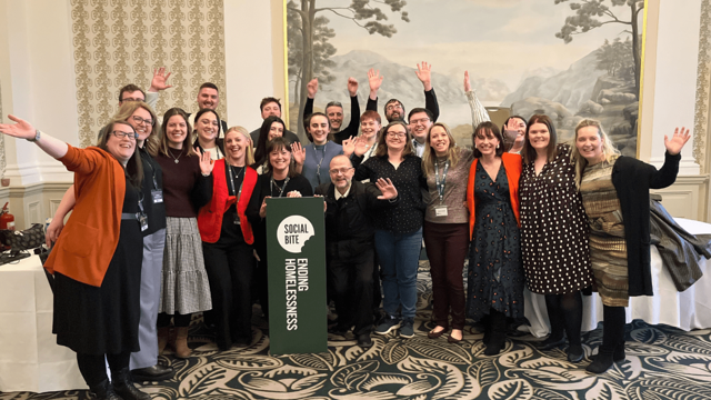 A group of people with arms raised celebrate in a room with a fancy carpet