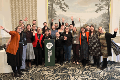 A group of people with arms raised celebrate in a room with a fancy carpet