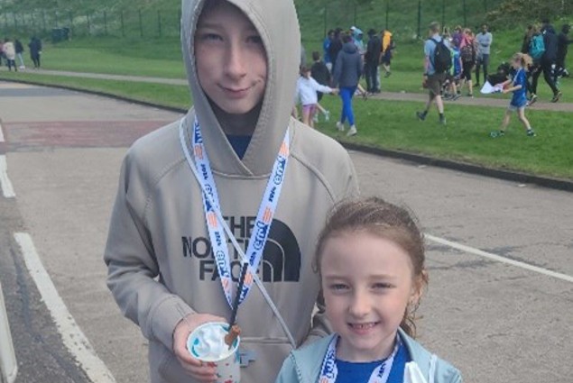 Two children eat ice creams. They're wearing medals and running gear