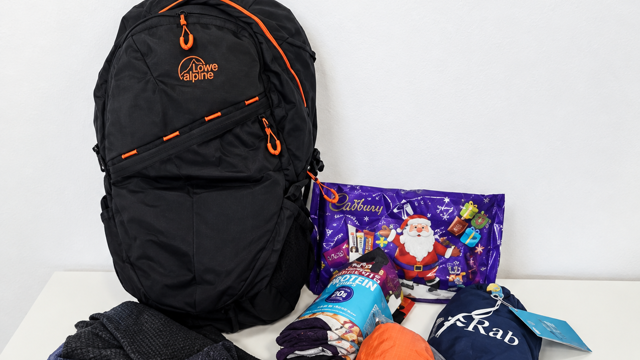 A black backpack on a white background. The contents of the bag is around it and makes up the winter essentials backpack. 