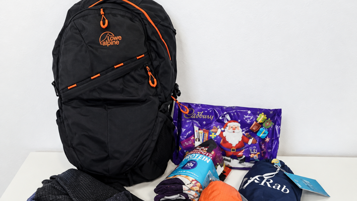 A black backpack on a white background. The contents of the bag is around it and makes up the winter essentials backpack. 