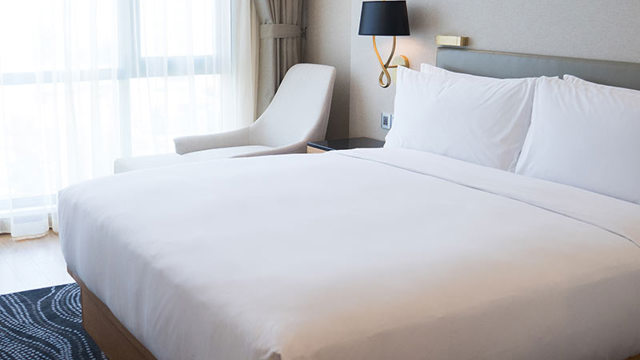 Photo of a double bed with white sheets and a chair by the side. 