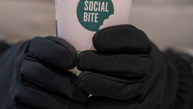 Hands wearing warm gloves holding a Social Bite coffee cup