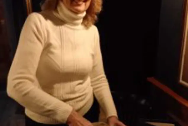 A woman in a white jumper smiling and pouring juice from a glass bottle