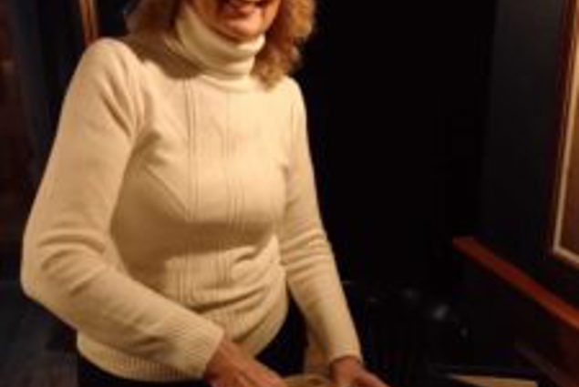 A woman in a white jumper smiling and pouring juice from a glass bottle
