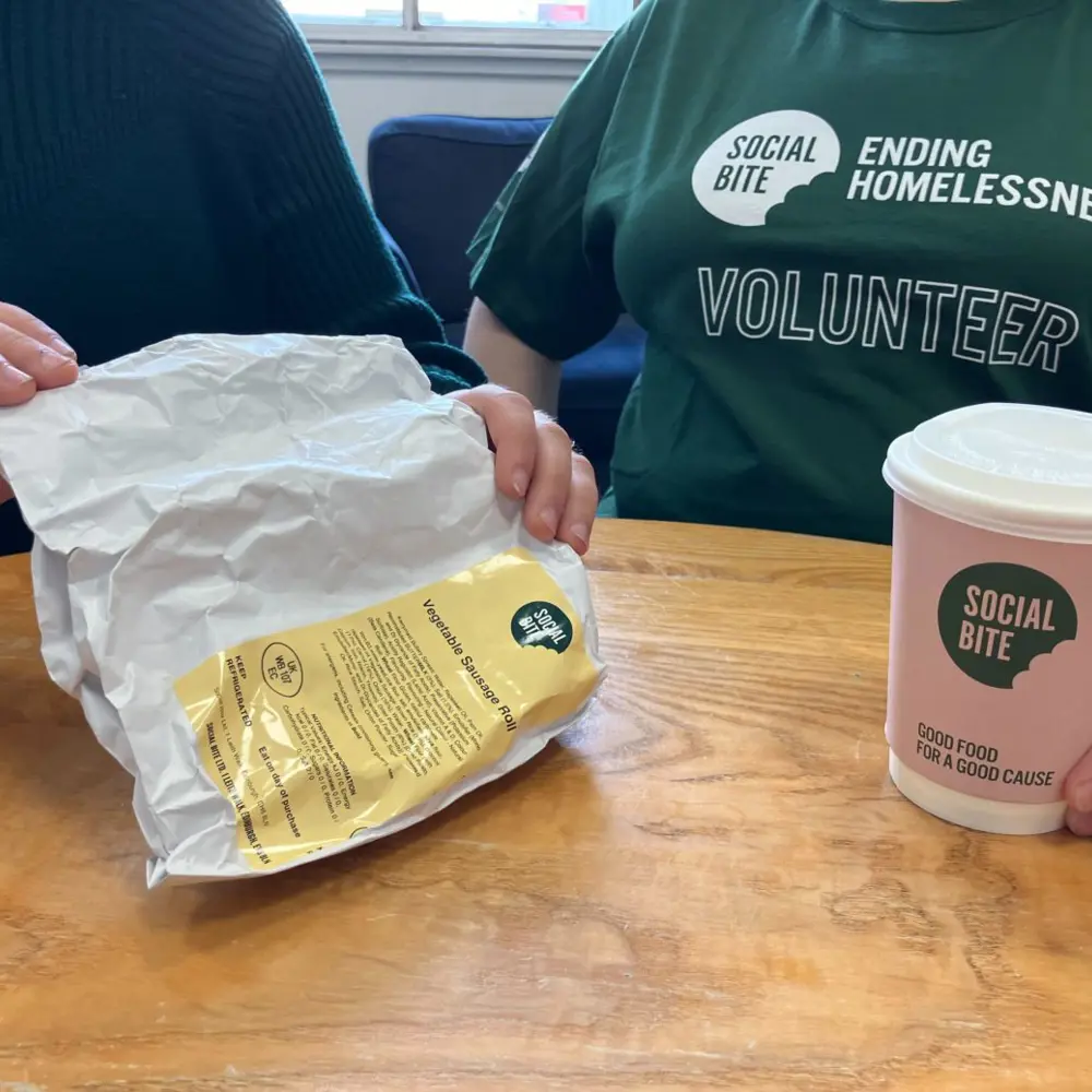 Two people sit together with a coffee. One wears a green tshirt that says volunteer.