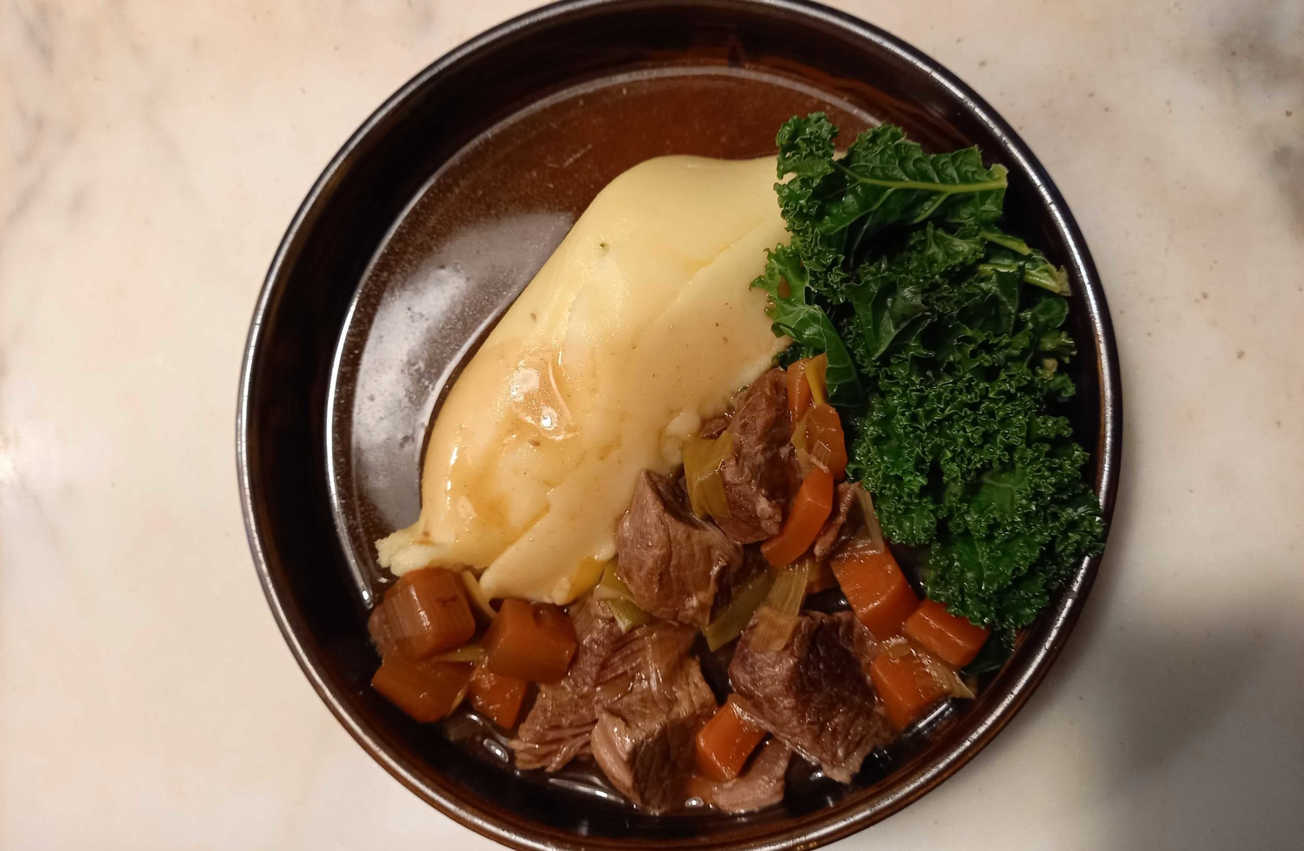 A round bowl with mashed potato, kale, beef stew and gravy