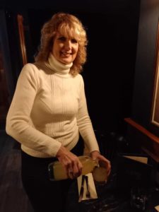 A woman in a white jumper smiling and pouring juice from a glass bottle