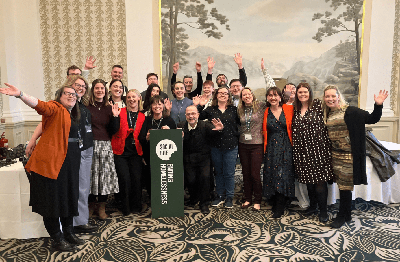 A group of people with arms raised celebrate in a room with a fancy carpet