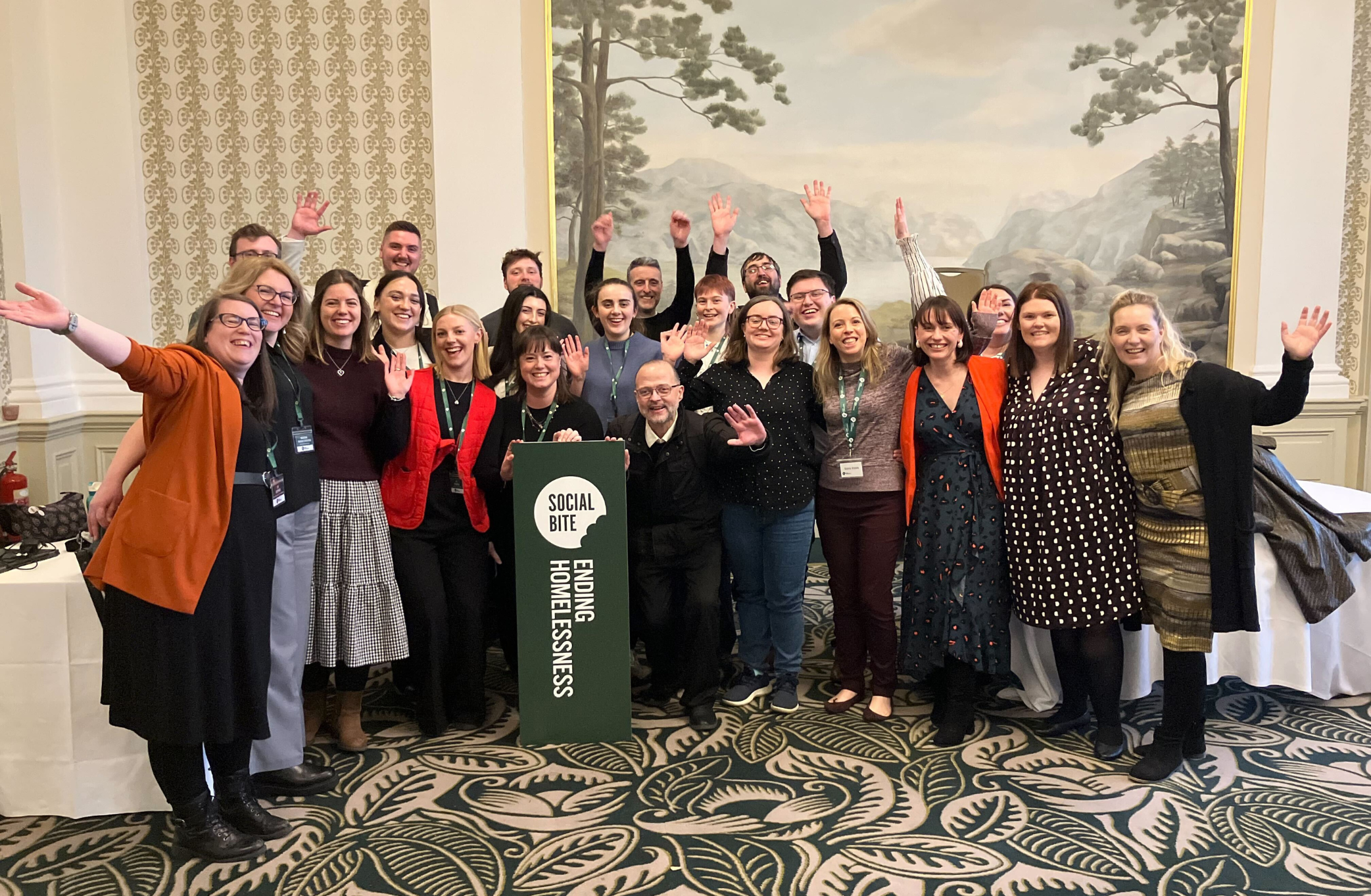 A group of people with arms raised celebrate in a room with a fancy carpet